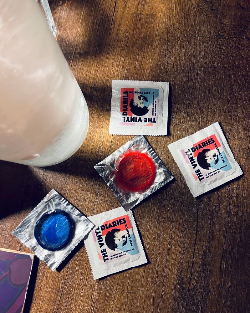 A scattering of condoms on a table. The cover image for The Vinyl Diaries is printed on them. 