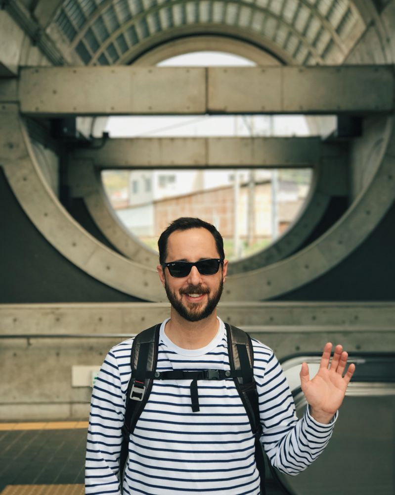 Me waving with the circular concrete of Uji Station in Japan in the background. 
