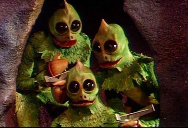 Green sleestak creatures from the 1970s TV show Land of the Lost, with a yellowish sagittal crest and big round dark eyes.