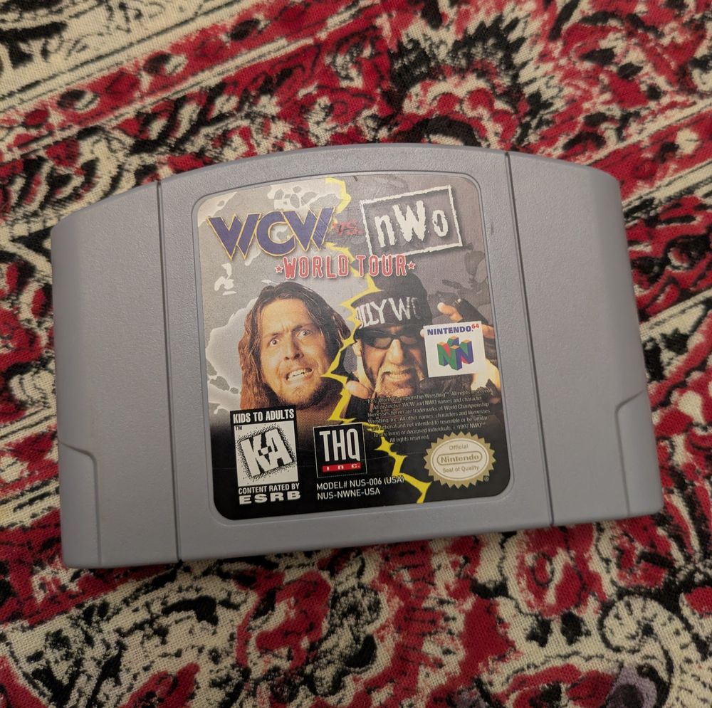 WCW Vs NWO World Tour cartridge for the Nintendo 64. The cartridge is resting on top of a red, black, and white patterned tablecloth.