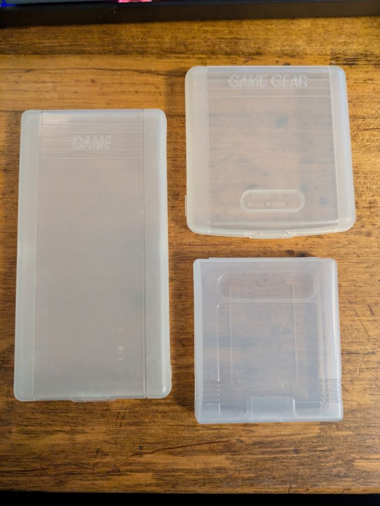 Three translucent plastic cases for handheld games, including one for Sega Game Gear, one for Nintendo Game Boy, and one for the weird SUPER GAME 15 in 1 bootleg cartridge.