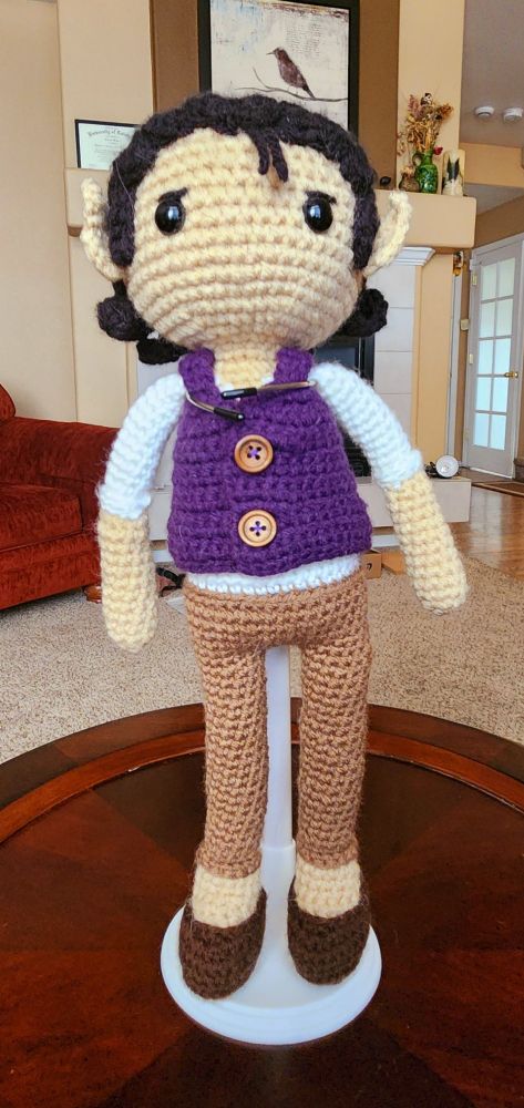 Crochet elf doll with a white undershirt, purple vest, brown pants, and brown shoes. His hair is black and pushed back and he has some slightly concerned eyebrows.