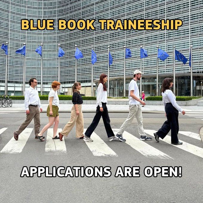 Six Blue Book Trainees are walking across a zebra crossing in front of the European Commission building in Brussels. EU flags are visible in the background. Bold yellow text at the top reads "BLUE BOOK TRAINEESHIP" and bold white text at the bottom reads "APPLICATIONS ARE OPEN!"