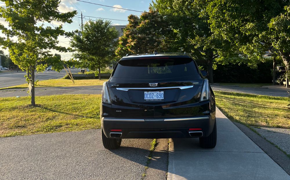 A giant Cadillac SUV is parked half across the sidewalk on a suburban street. To the left and right is space on the driveway where it could park instead without blocking the sidewalk.
