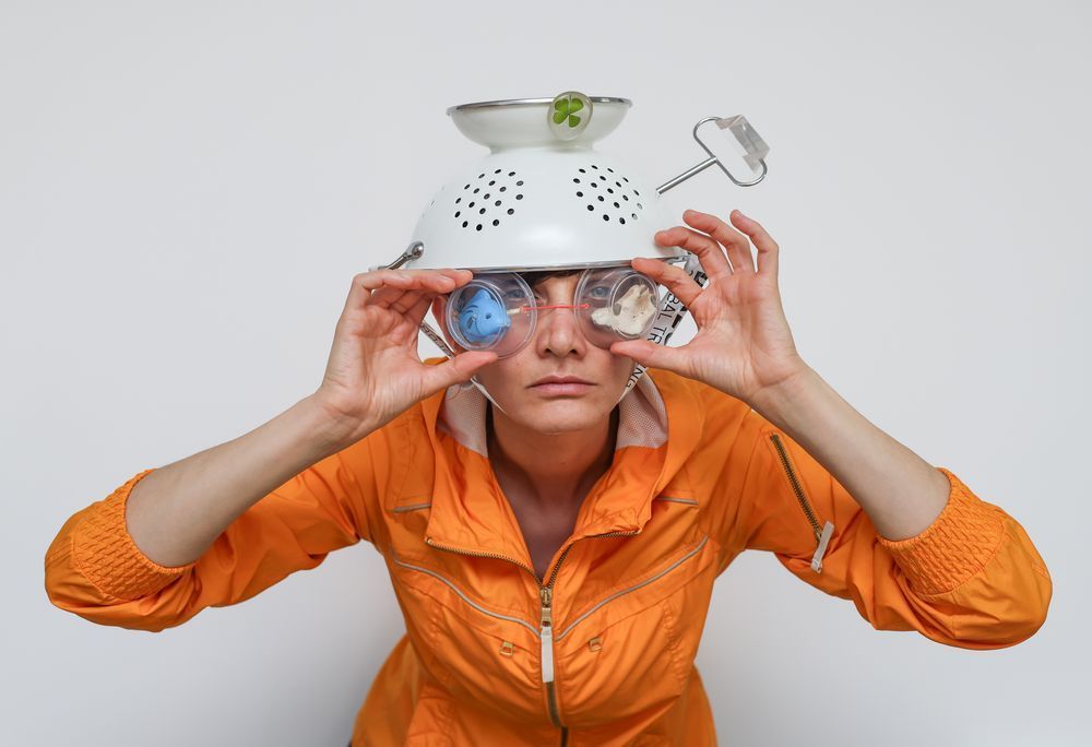 Solmaz in an orange suit, with a strainer upside down on her head, holding goggle over her eyes
