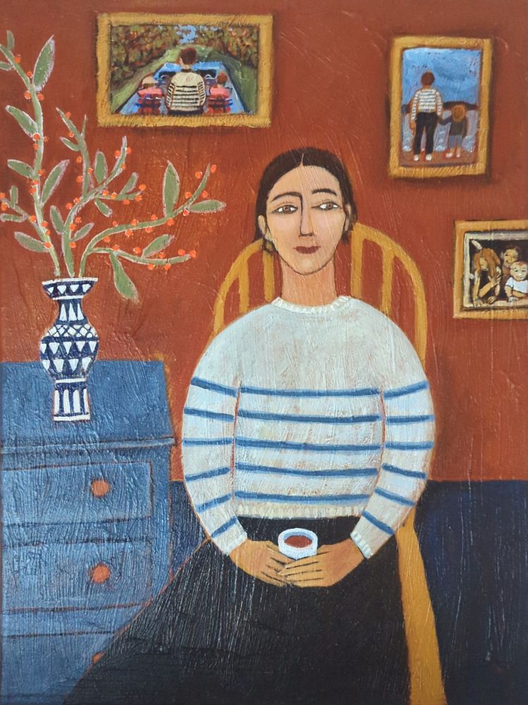 Portrait of a woman in a Breton jumper holding a cup of coffee, she is surrounded by family photos. 