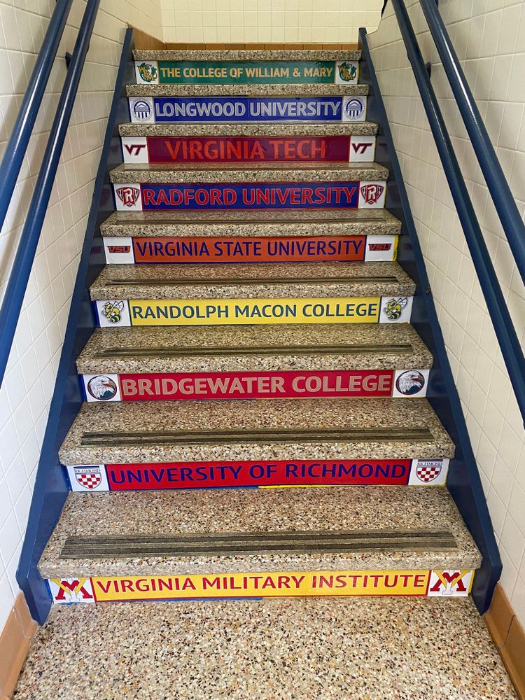 A photo of a staircase. The front of each step has a sticker with the name and logo of a college or university in Virginia.