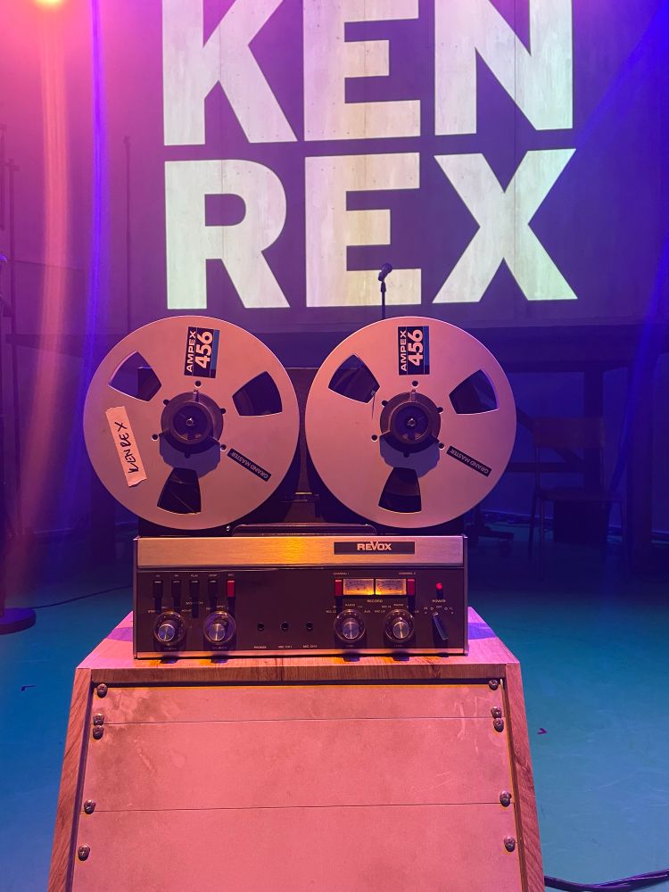 Set of the play Kenrex with an old fashioned tape reel and the letters KENREX behind it. 