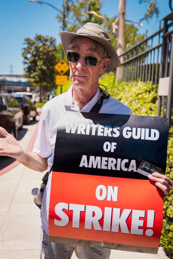 Bill nye of the picket line holding a WGA sign and his SAG union card 