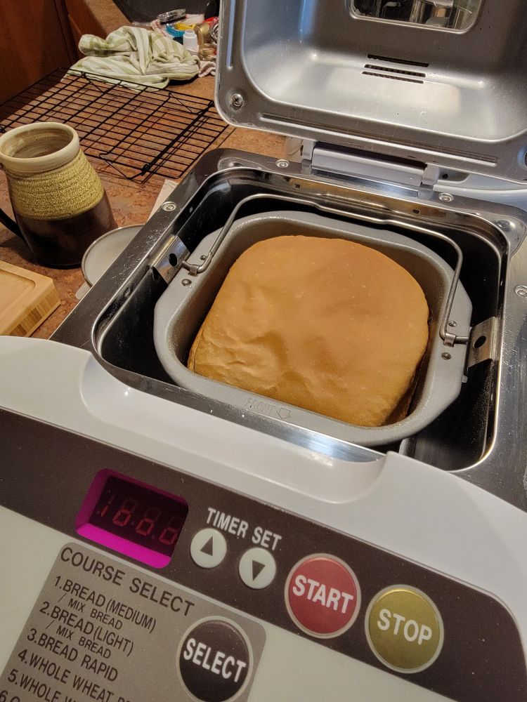 A loaf of bread in an open bread machine. Text in foreground is the operations and buttons for the machine.
