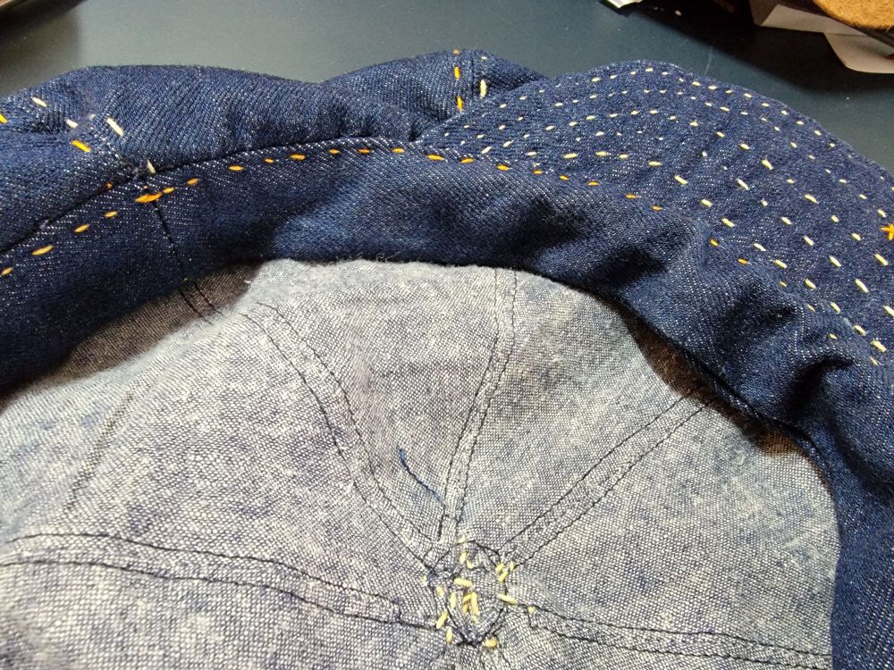 Interior closeup of a dark blue denim newsboy cap showing the light blue linen lining.