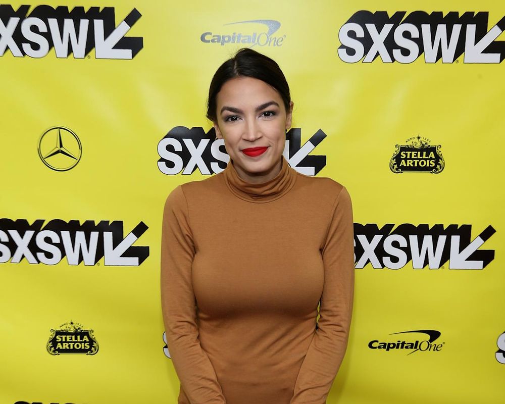 Alexandria Ocasio-Cortez, looking radiant in a long-sleeve brown turtleneck, hair pulled back.