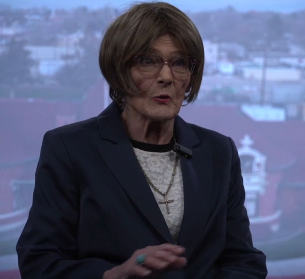 Nampa mayoral candidate Suzi Robinson, an older white woman with glasses in a blue blazer, white blouse, and prominent crucifix necklace.
