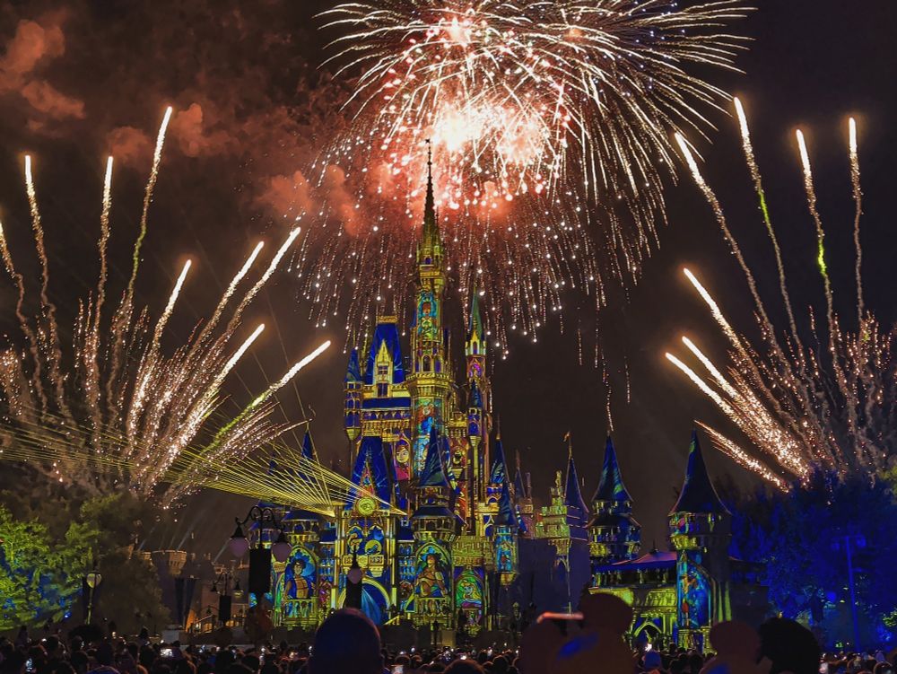 Yellow and white fireworks blasting above Cinderella Castle, streamers blasting to its sides.