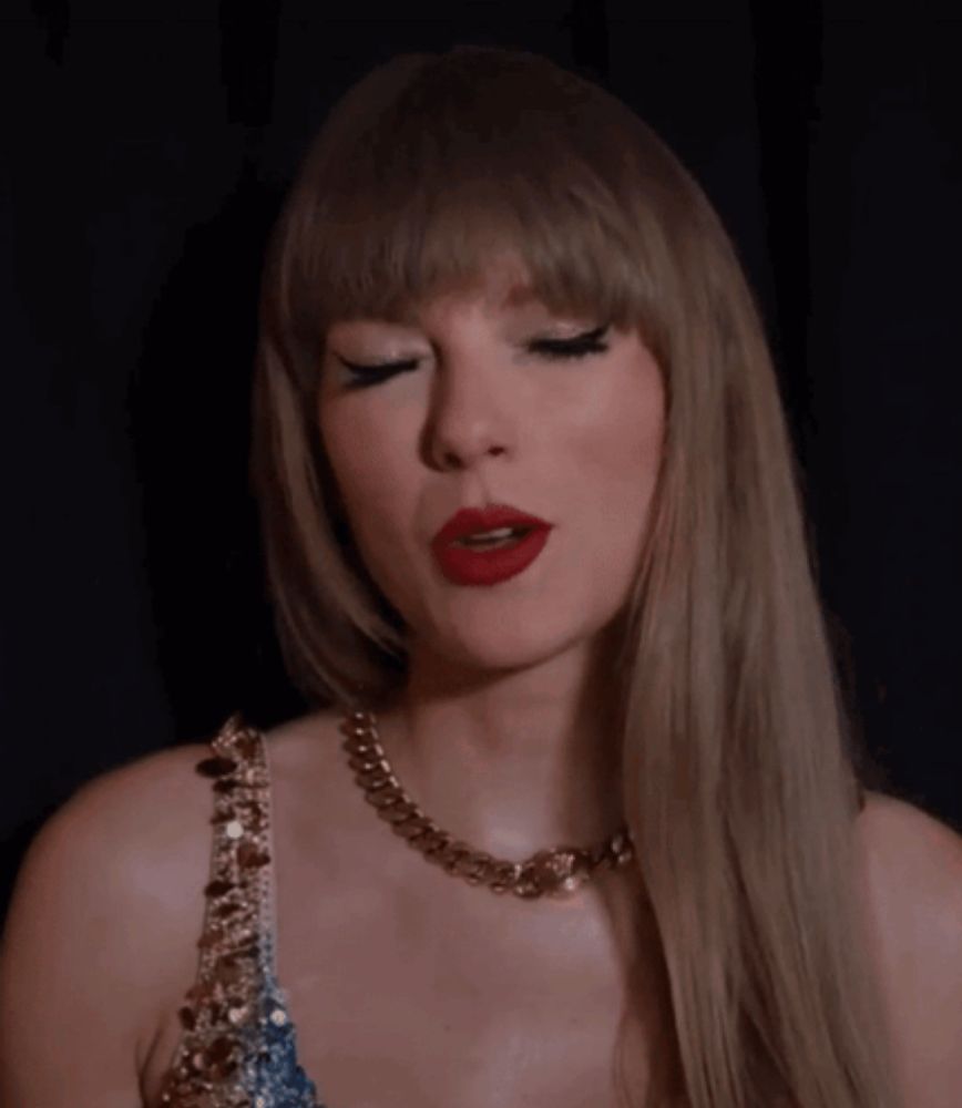 taylor swift is wearing a blue dress and a gold chain necklace .