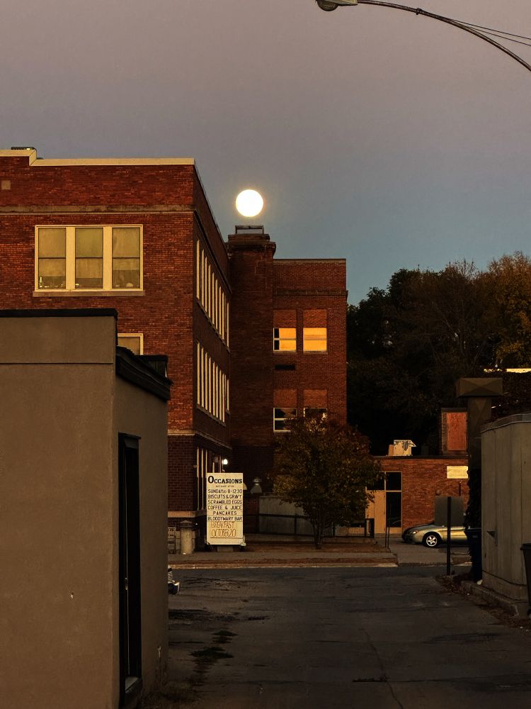 Photo of the moon positioned above a chimney stack on an old school building. 