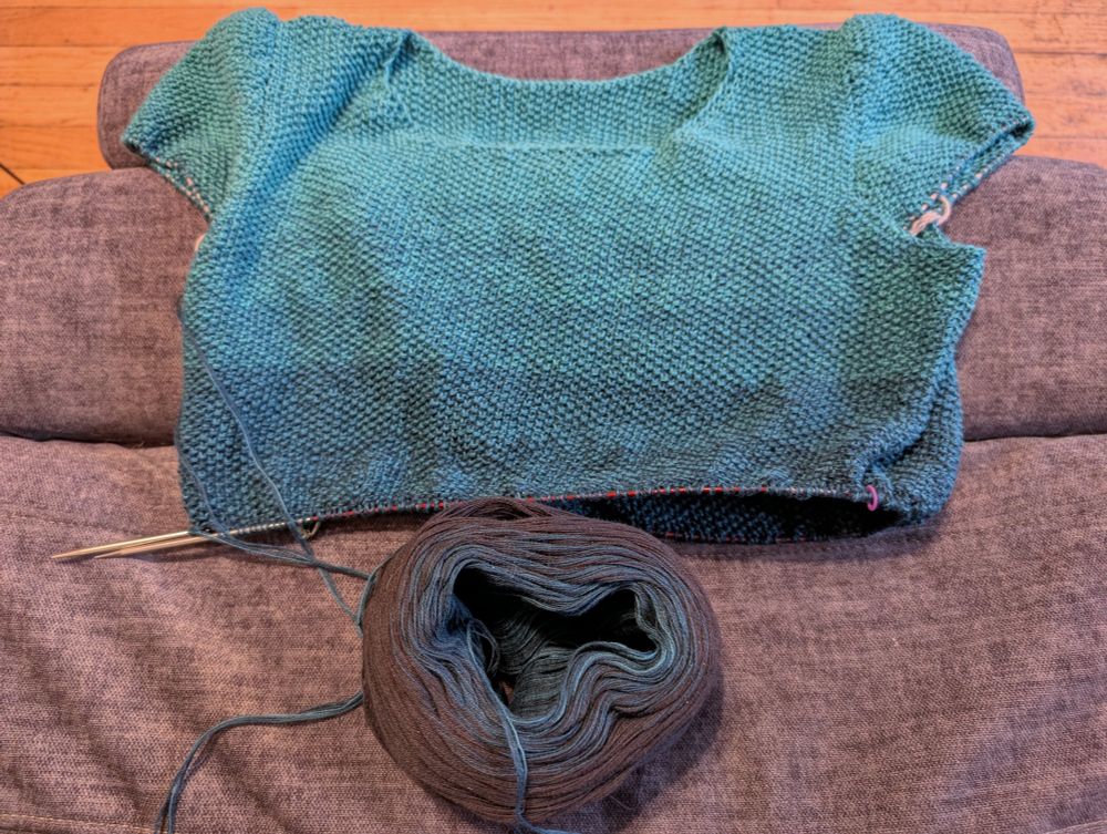A teal t-shirt in the process of being knitted.