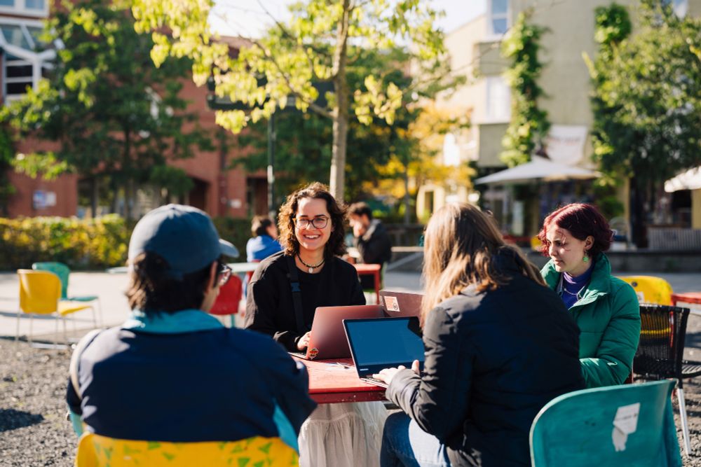 Studierende sitzen mit Laptops um einen Tisch im Freien in der Herbstsonne