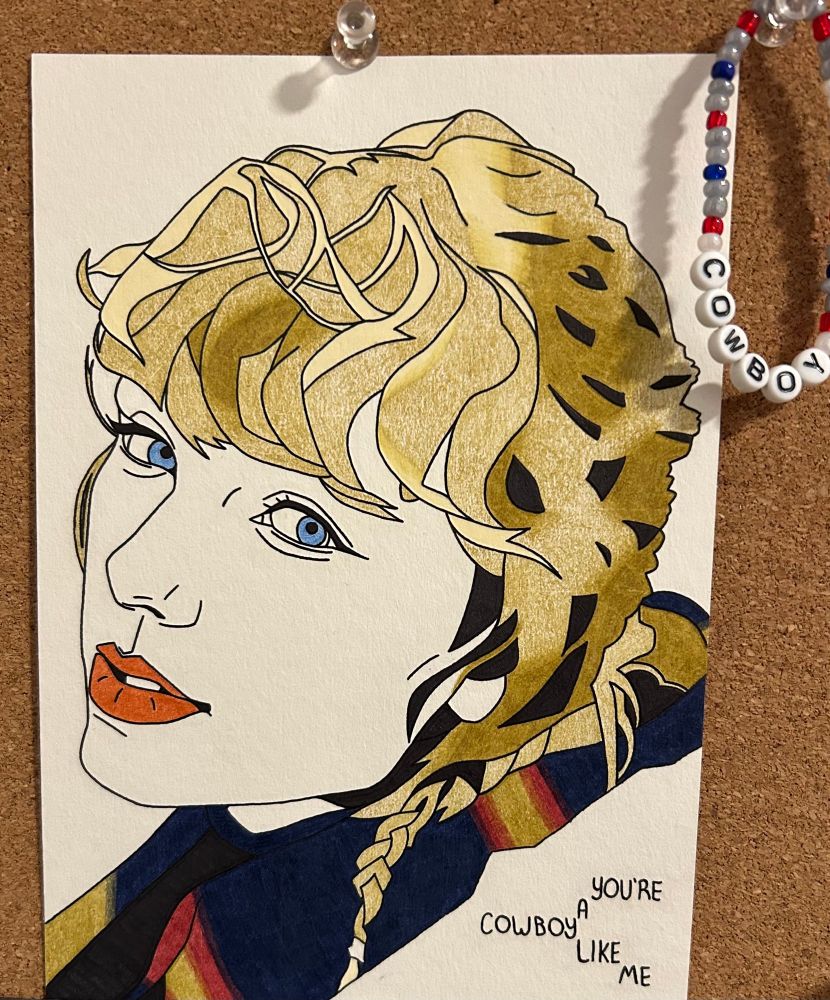 Hand drawn picture of Taylor Swift from the Evermore shoot with the lyrics “you’re a cowboy like me” written on it. A bracelet with the word “cowboy” is hanging next to it on a bulletin board.