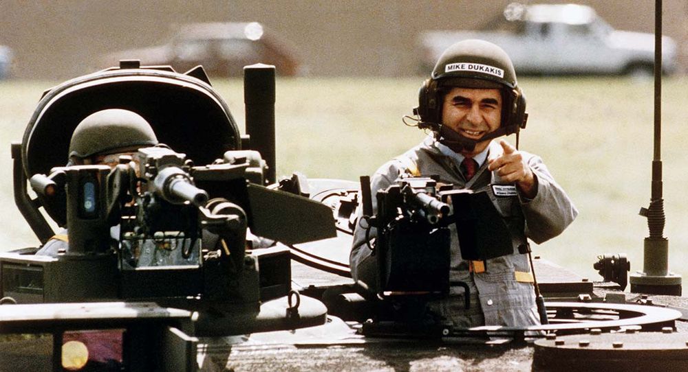 The image show Dukakis in a military tank during a photo opportunity. He's wearing a helmet with headphones while smiling and pointing from the tank's turret. This infamous photo op became a political liability and damaged his campaign.

