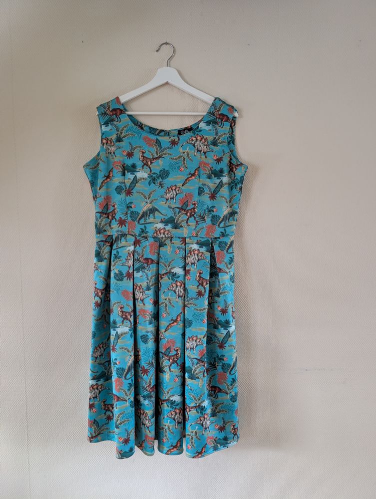 En turkis, ermeløs kjole med fargerikt dinosaurprint. 