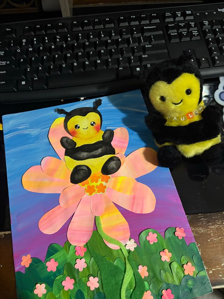 the bee plushie in real life sitting next to the art piece on my desk, with a keyboard in the background