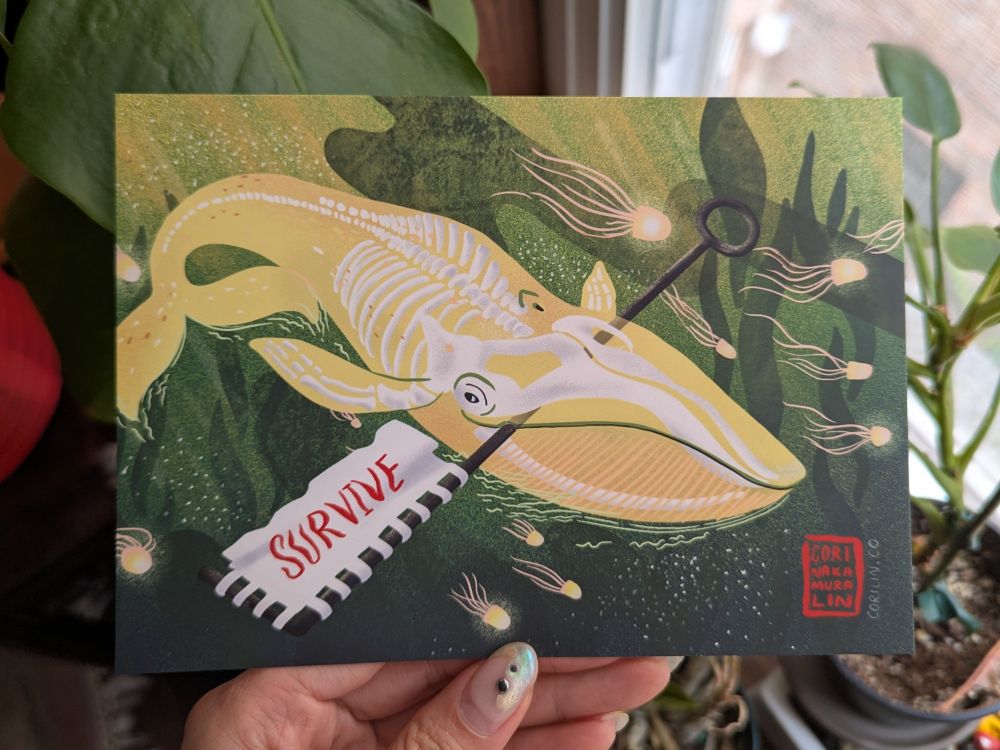 Hand holding an 5x7 illustrated postcard of a yellow ghost whale holding a flag that says SURVIVE in red. The ghost whale is surrounded by jellyfish and kelp