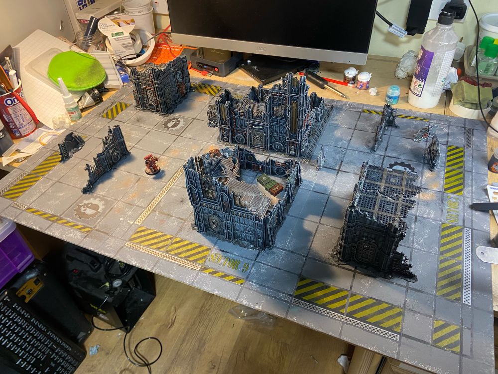 Scratch built Killteam base baseboard of a paved industrial area with hazard stripes and cogs mechanicus painted on the slabs. Painted in shades of grey with silver and copper metallics, the HiveStorm terrain pieces have been placed upon it.