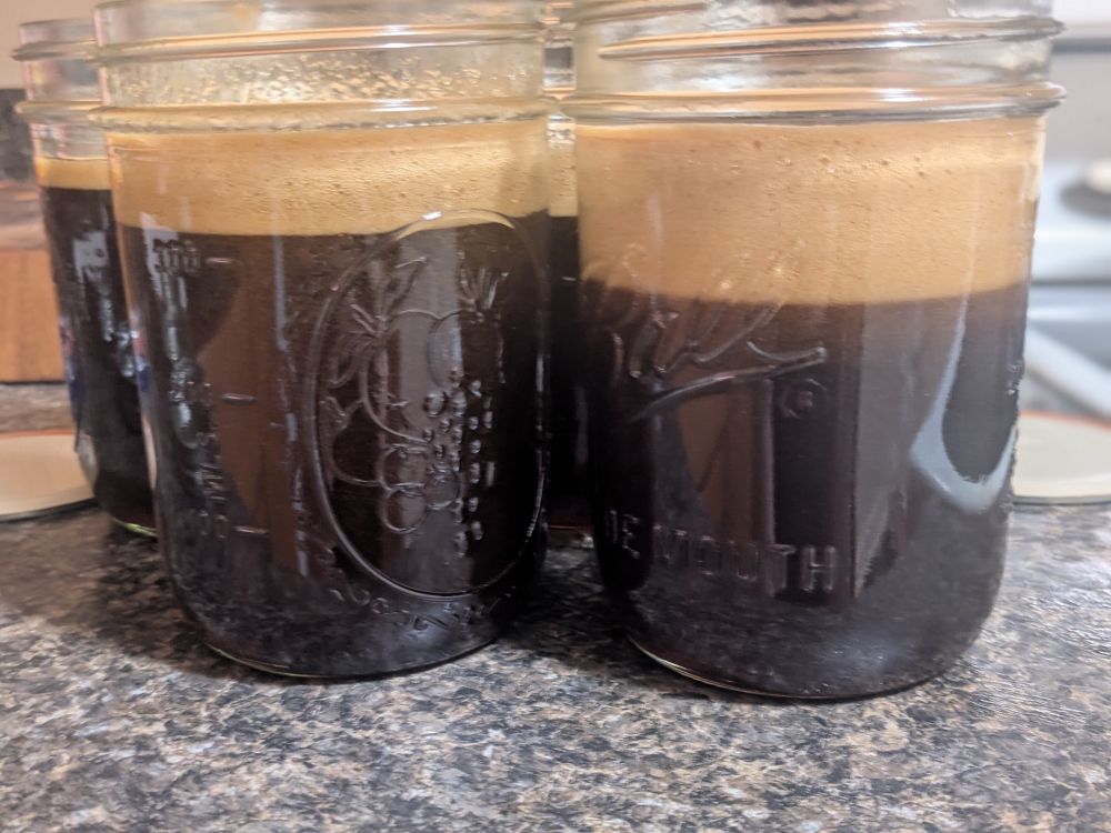 Some mason jars of a caramelized honey. The jars are nearly full of an extremely dark amber liquid with an inch or more of a brown foam on top.