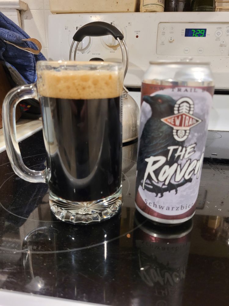 can of new trail brewing's the raven with a picture of a raven on it, next to an extremely dark beer in a mug