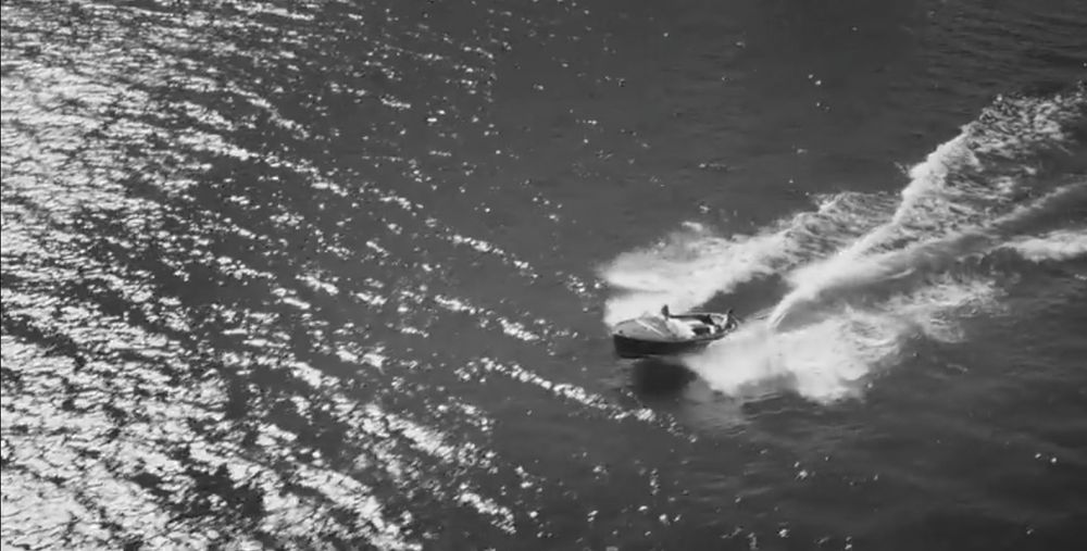 Ein Screenshot aus dem Musikvideo 'Espresso' von Sabrina Carpenter. Man sieht, wie ein Motorboot über einen See fährt. Die Szene ist in schwarz-weiß