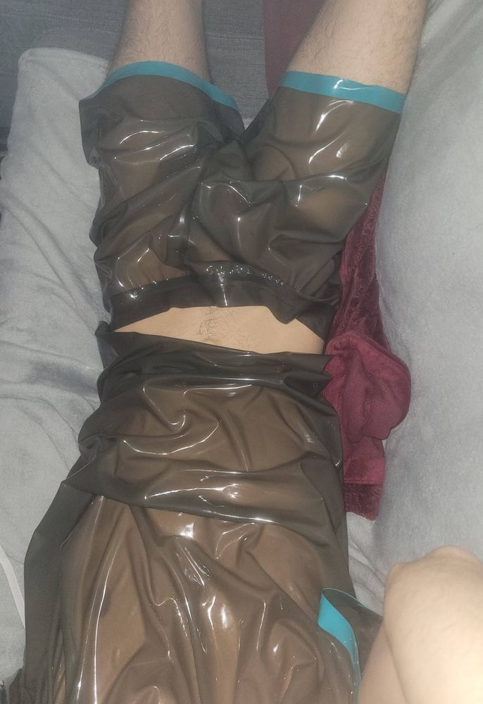 Boy laying on couch wearing smoky trans latex pajamas.
