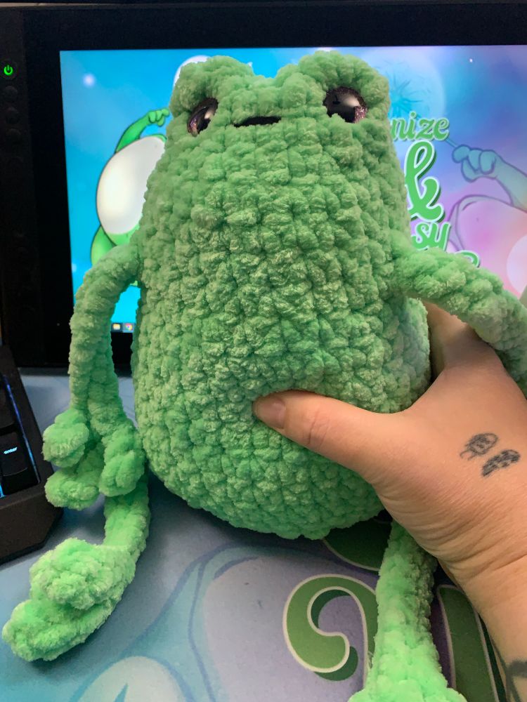 A hand holding a fairly big squishy crocheted frog stuffy
