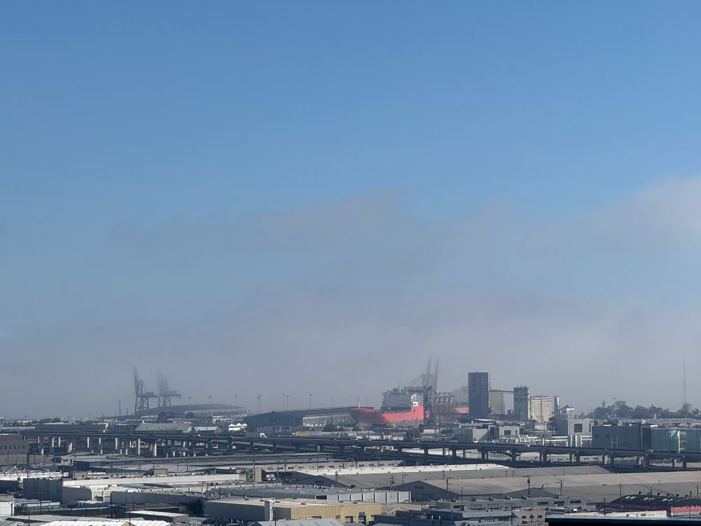 The bay past the industrial zone, shrouded in fog, clear blue sky above, San Francisco