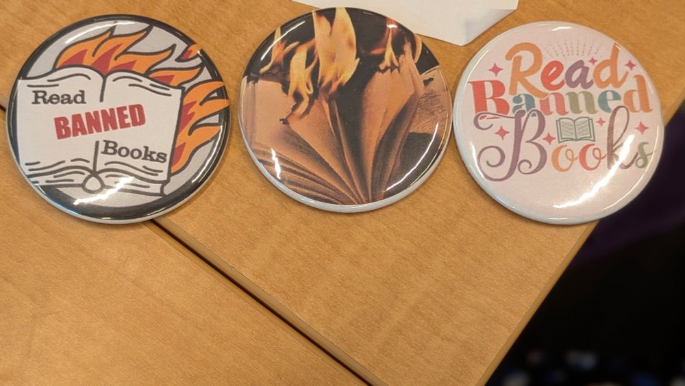 Three round magnets with book and flame themes, promoting reading banned books.