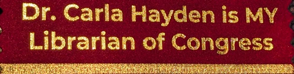 A crimson conference ribbon and gold lettering that says "Dr. Carla Hayden is MY Librarian of Congress."
