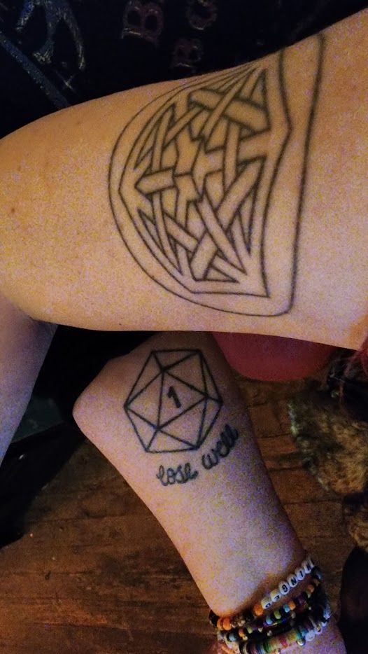 my black line art upper arm everything (game) logo tattoo, six-pointed interconnected sacred geometry encased in a circle, photographed at an understandably awkward angle against a tattoo of the same size on someone else's inner arm depicting a 20-sided die with a 1 on the top face and the script "lose well"
