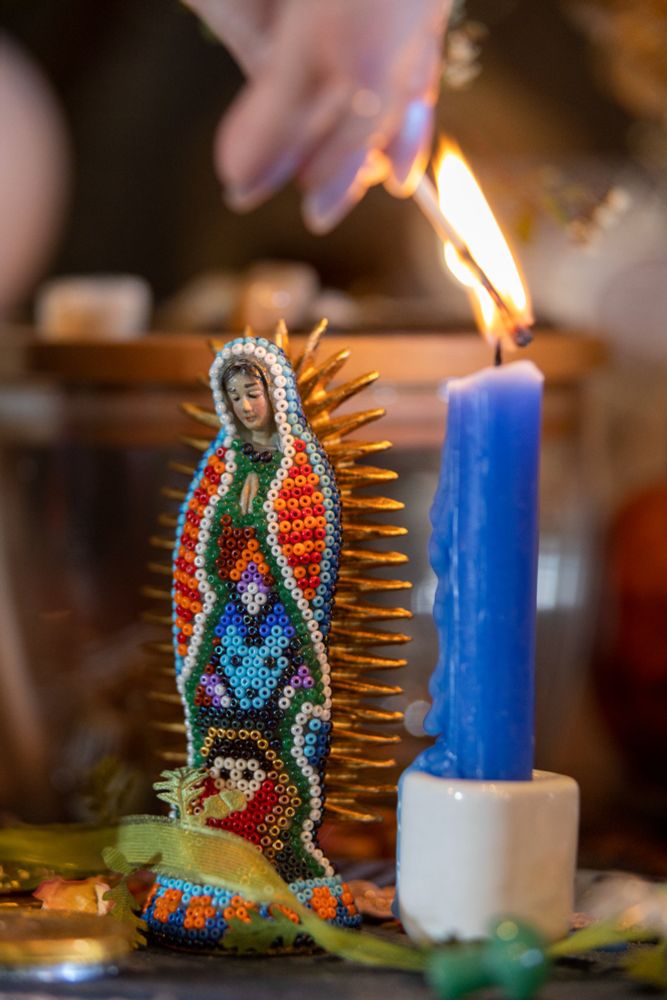 Closeup view of a match lighting a blue candle. There is a beaded virgen de guadalupe right next to the candle.