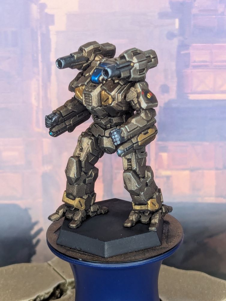 A miniature of a Tian-zong battlemech, painted in bronze and gold metallic colors, with a blue cockpit and an attempt at a unit marking on one shoulder.
