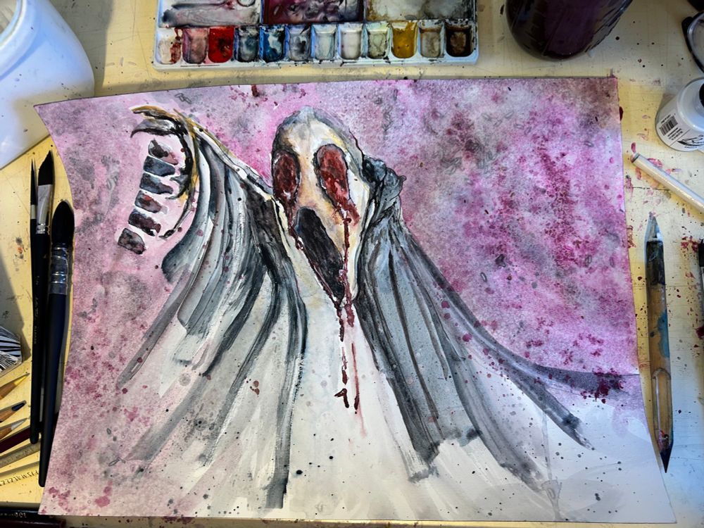 Watercolor painting of a haunting, ghost-like figure with skeletal features and dramatic, flowing wings set against a textured pink and crimson background. The figure’s face is partially obscured, with deep red accents resembling blood tears, evoking a sense of anguish and raw emotion. Surrounding tools and splattered paint hint at the creative process behind the artwork.