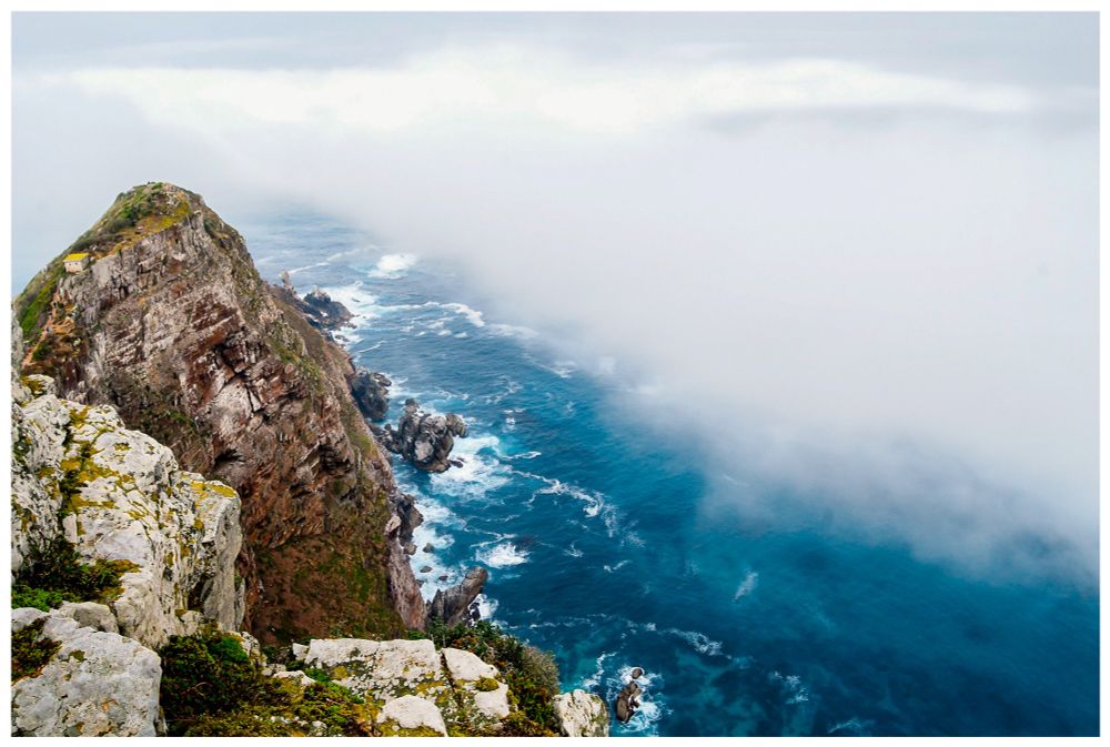 Photograph of the rocky cliffs, turbulent azure waters, and endless misty clouds on the southern coast of Africa. (Not the true southernmost point, but it feels that way as you gaze across the abyss toward Antarctica)