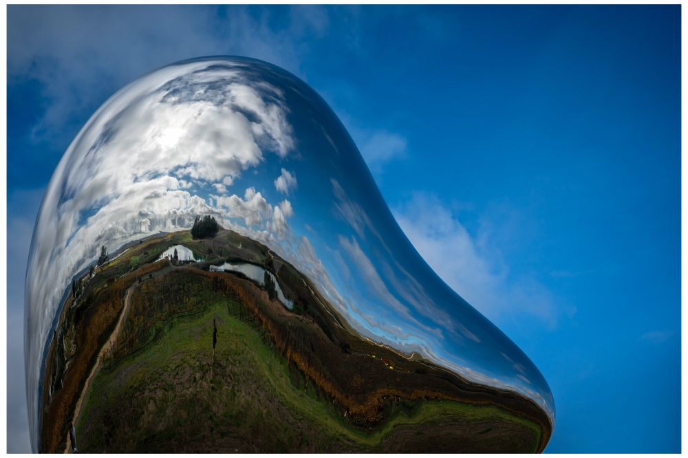 The autumn landscape - vineyards, ponds, rolling hills, fluffy clouds and a brilliant blue sky - are reflected in a metallic, rounded sculpture set against the same blue sky. 

Photo taken at Donum Estates, Sonoma, CA. 

Sculpture: “Love Me” by Richard Hudson, 2016