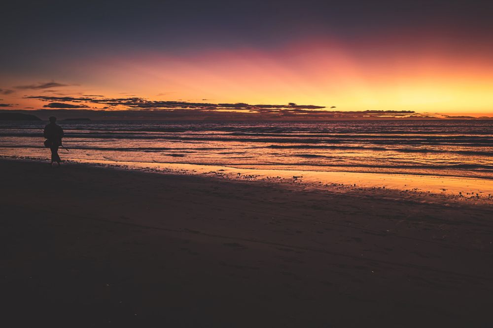 The beach glows in the golden pink glow of sunrise. A lone fisherman walks barefoot along the wet sand, pole in hand. If only all mornings were this peaceful. 