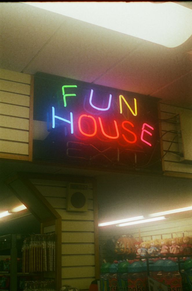 A multicolored neon sign in a souvenir/clothing store reading "FUN HOUSE EXIT", but the portion reading exit is not lit (broken? Fire code? i can't say.)
