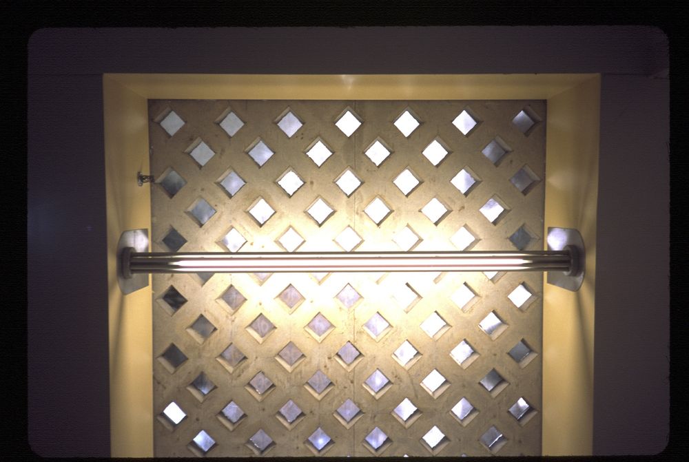 A light (in a bar shape, LED or fluorescent) reflects off a ceiling made of concrete in a lattice shape. A larger outside frame is made from the surrounding ceiling work.