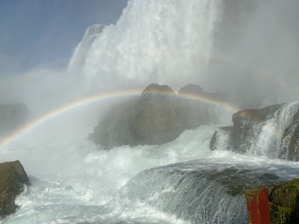 An image of several waterfalls at Niagara Falls from the bottom of the falls. A rainbow arcs across the photo. 