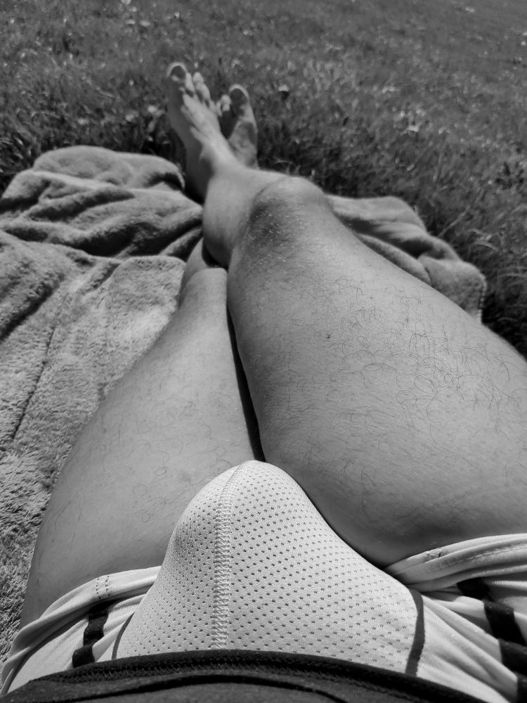 Me lying outdoors in the sun on a towel just wearing a shirt and some mesh underwear with a clearly visible bulge and my legs crossed. 