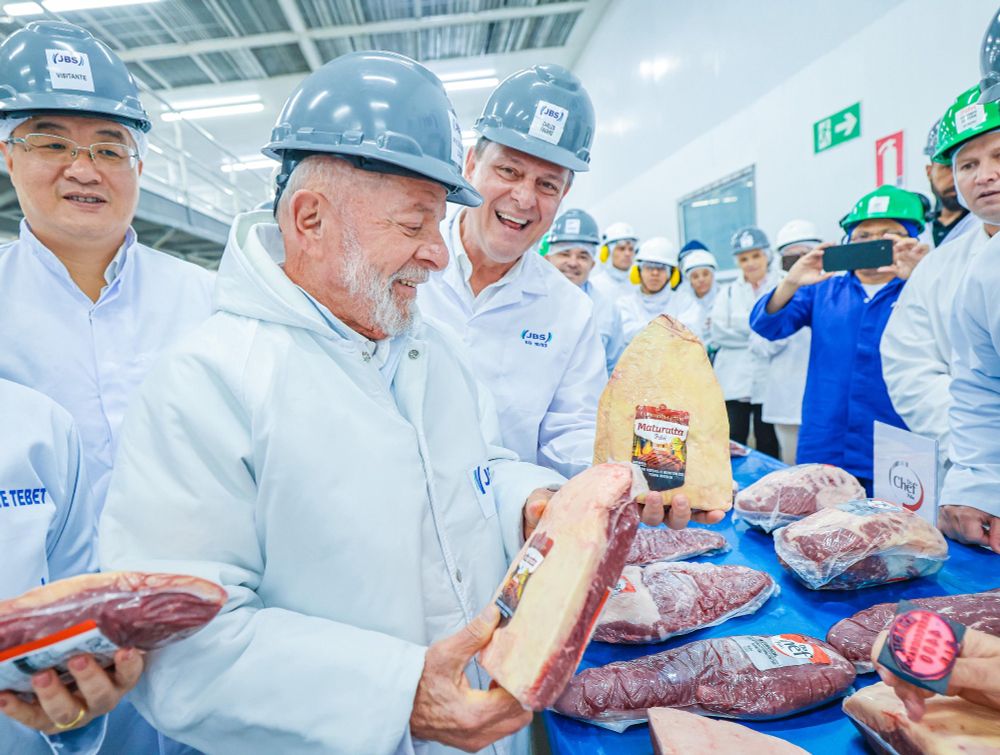 Presidente Lula segurando um pedaço de carne durante visita ao frigorífico em Campo Grande (MS). Ao lado, representantes da comitiva, da indústria e o ministro da Agricultura Carlos Fávaro.