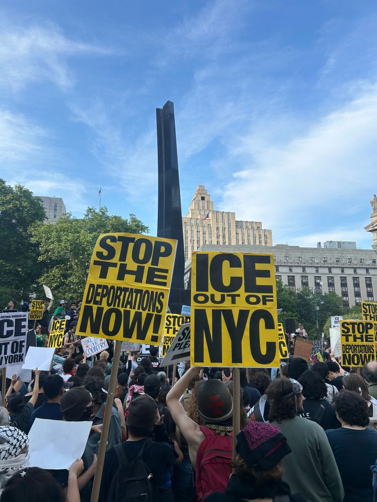 Photo of a large group of protesters holding yellow and black signs that say “ICE out of NYC” and “Stop the deportations now!”