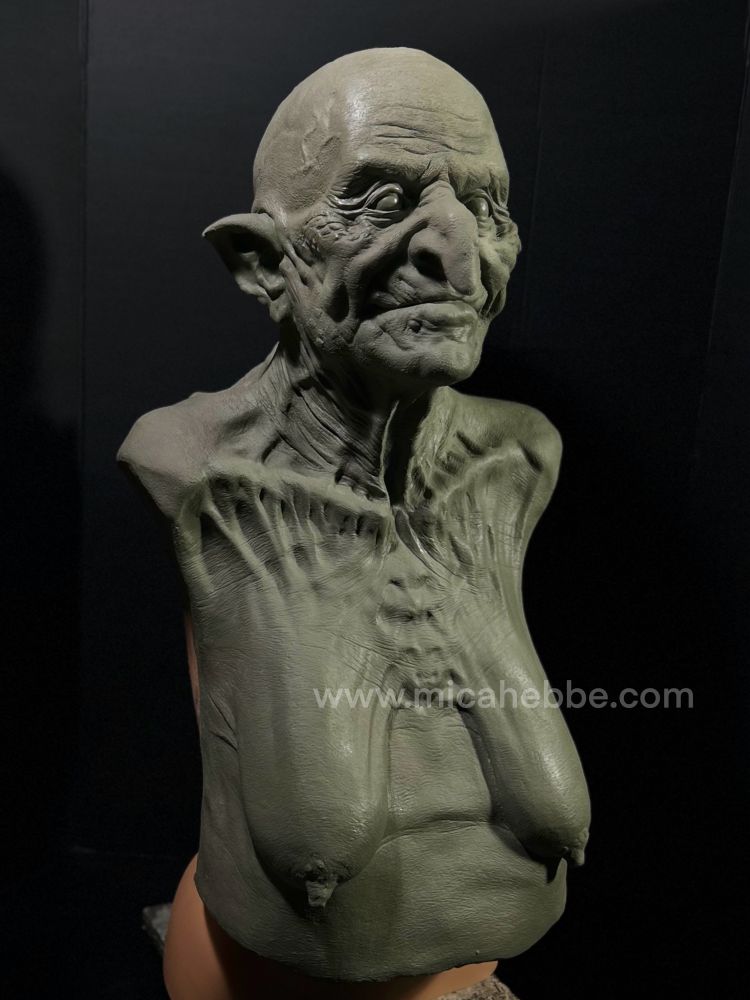 Clay sculpture of a witch from the waist up for a latex mask. She is naked and her skin is stretched over her bones. She has a slight smile. 3/4 view